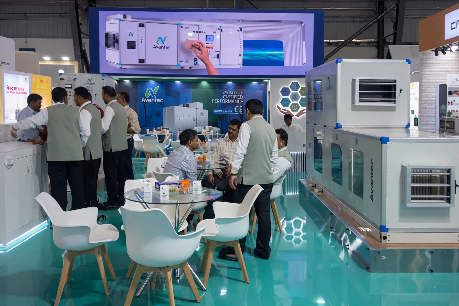 Trade show booth for Avantec with people in formal attire interacting and sitting around glass tables with white chairs.