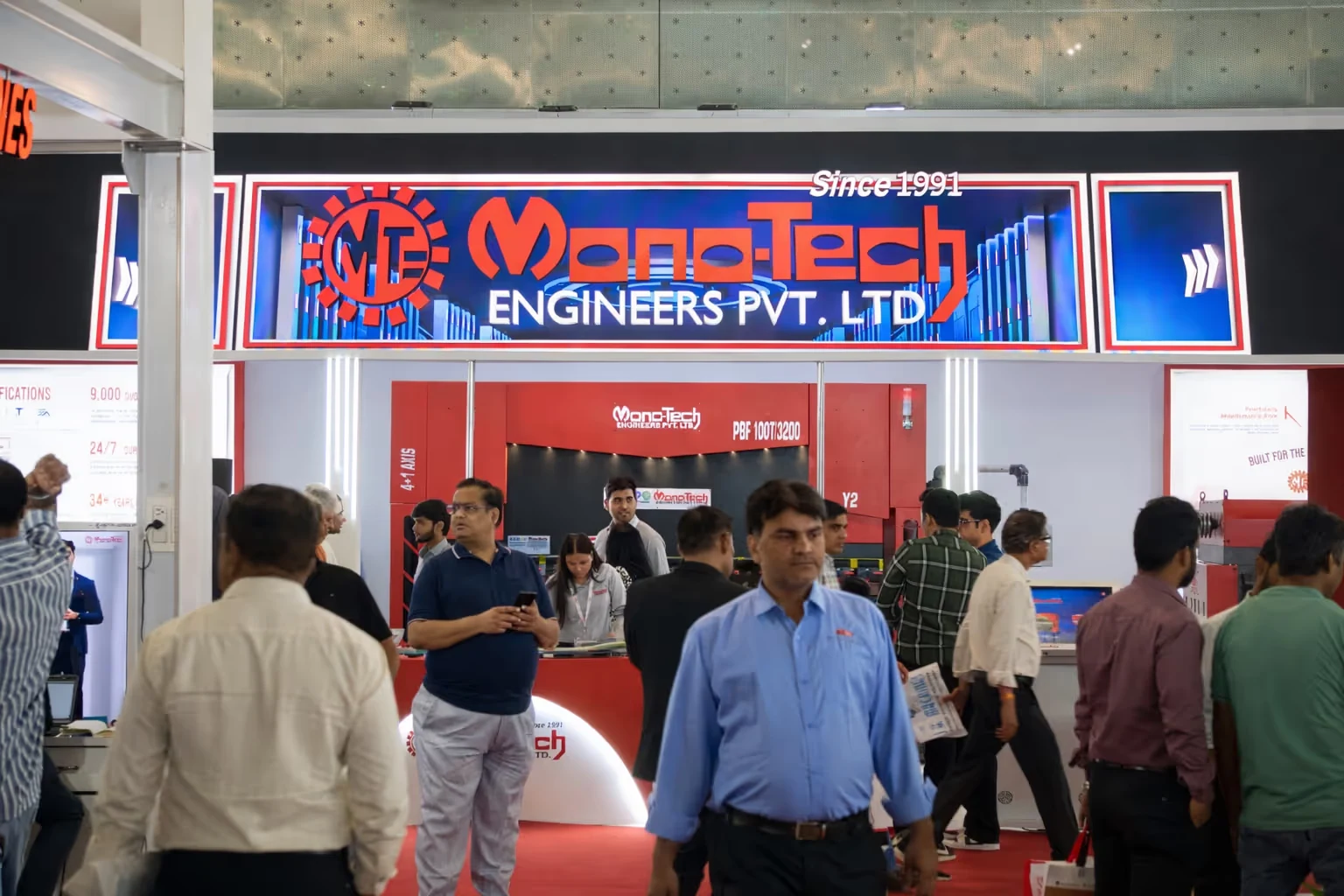 Busy exhibition booth of Mono-Tech Engineers Pvt. Ltd. with visitors in front and company signage overhead.