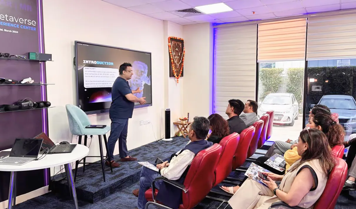 Presenter explaining metaverse concepts to seated audience in a modern conference room with a large screen display.
