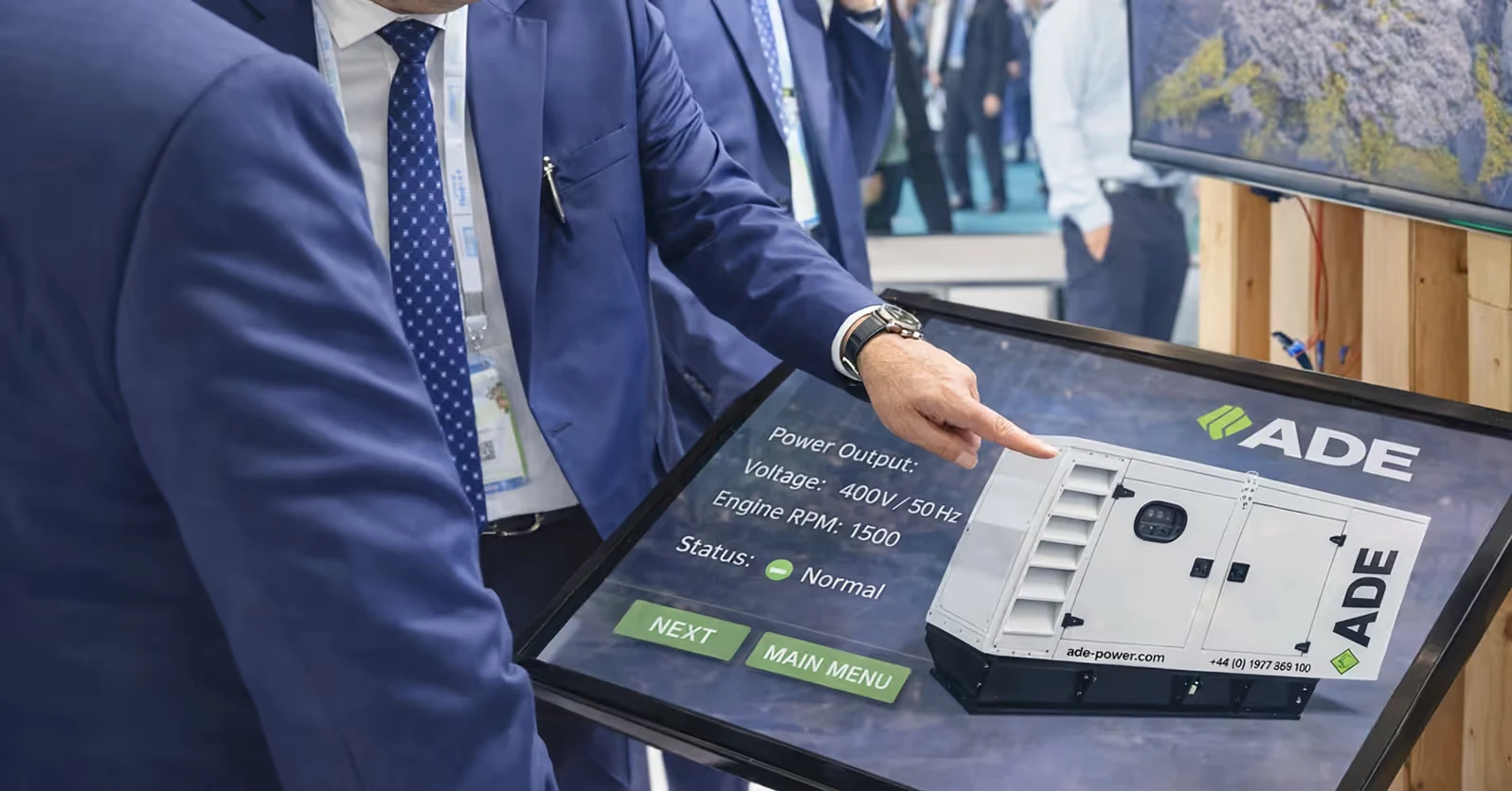 Man in blue suit pointing at touchscreen display showing technical details and image of an ADE generator.